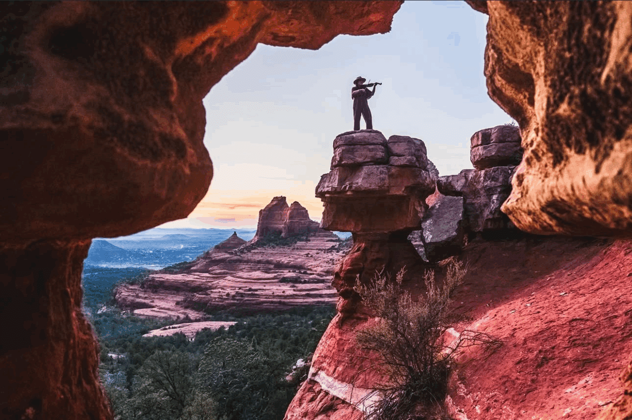 man playing violin on top of rock with cliff view